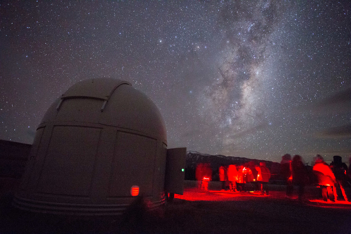 Group of stargazers looking upon the milky way in red lighting