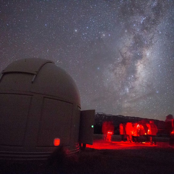 Group of stargazers looking upon the milky way in red lighting