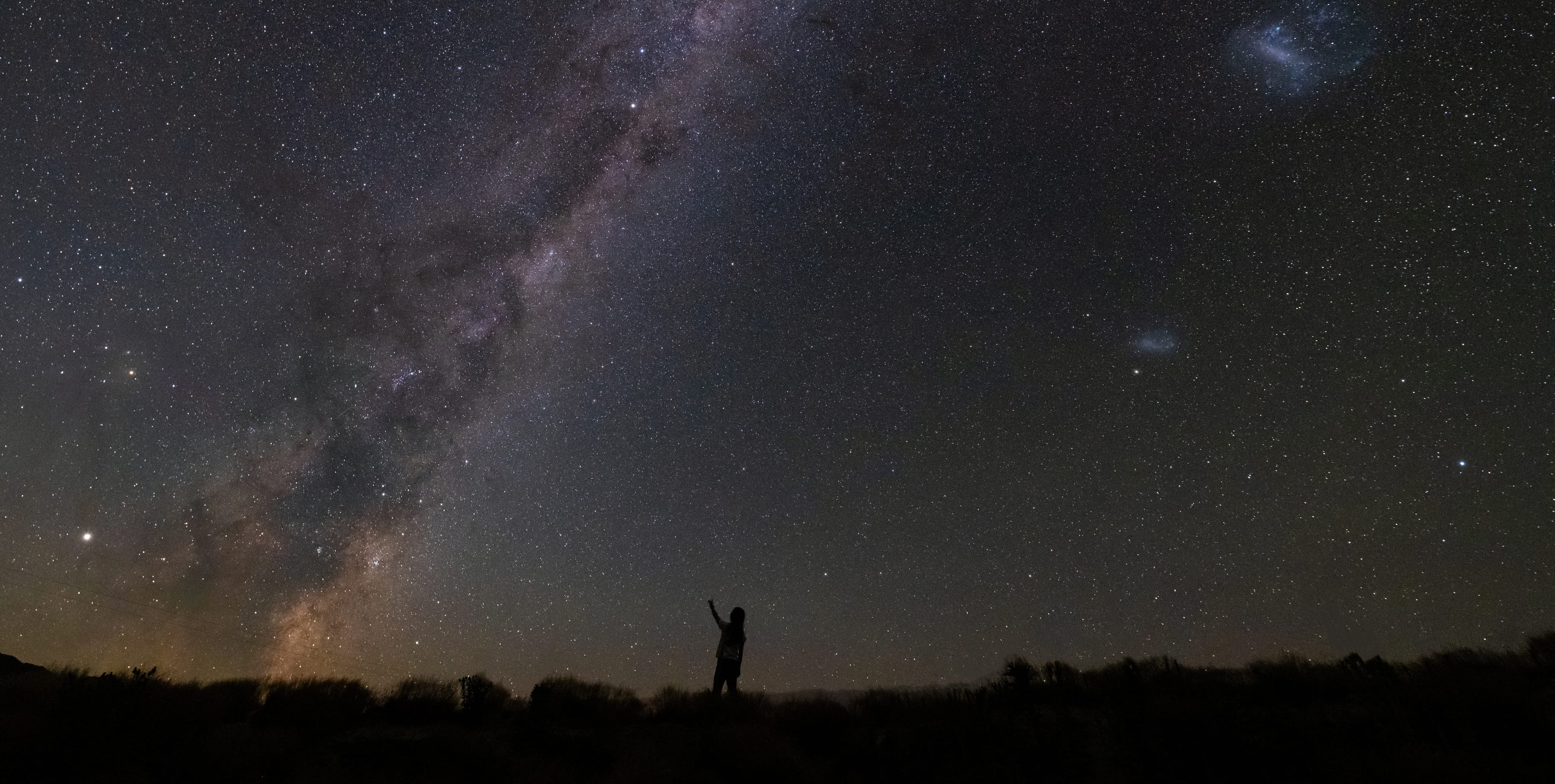 Person reaching up to the night sky with milky way in the sky
