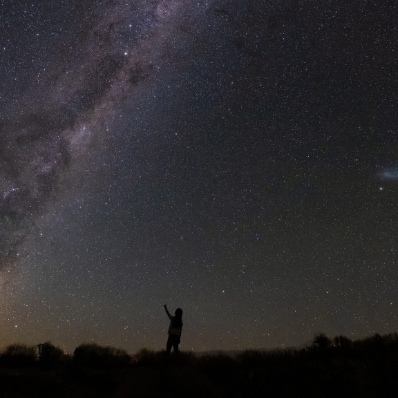 Person reaching up to the night sky with milky way in the sky