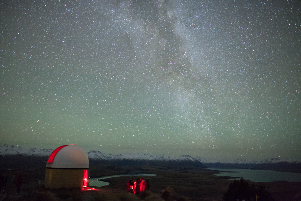 Red light spilling from observatory dome with snowy mountains and milky way