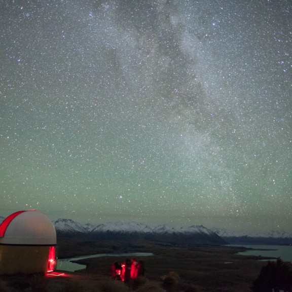 Red light spilling from observatory dome with snowy mountains and milky way