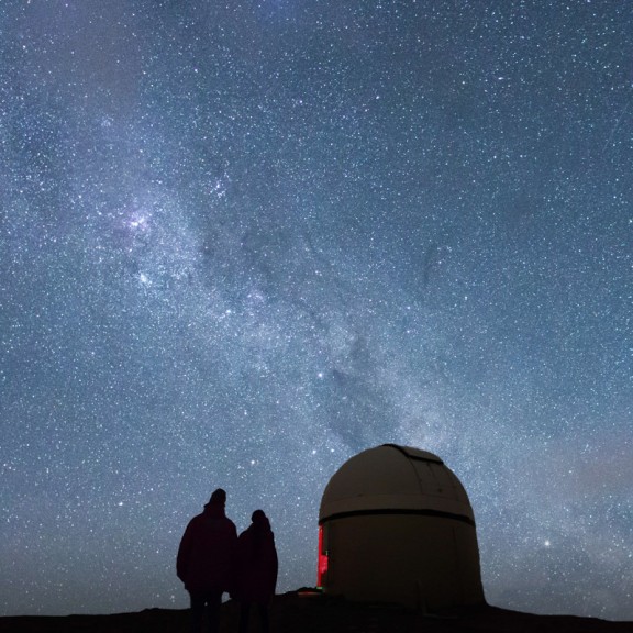 Couple next to observatory dome with milky way above