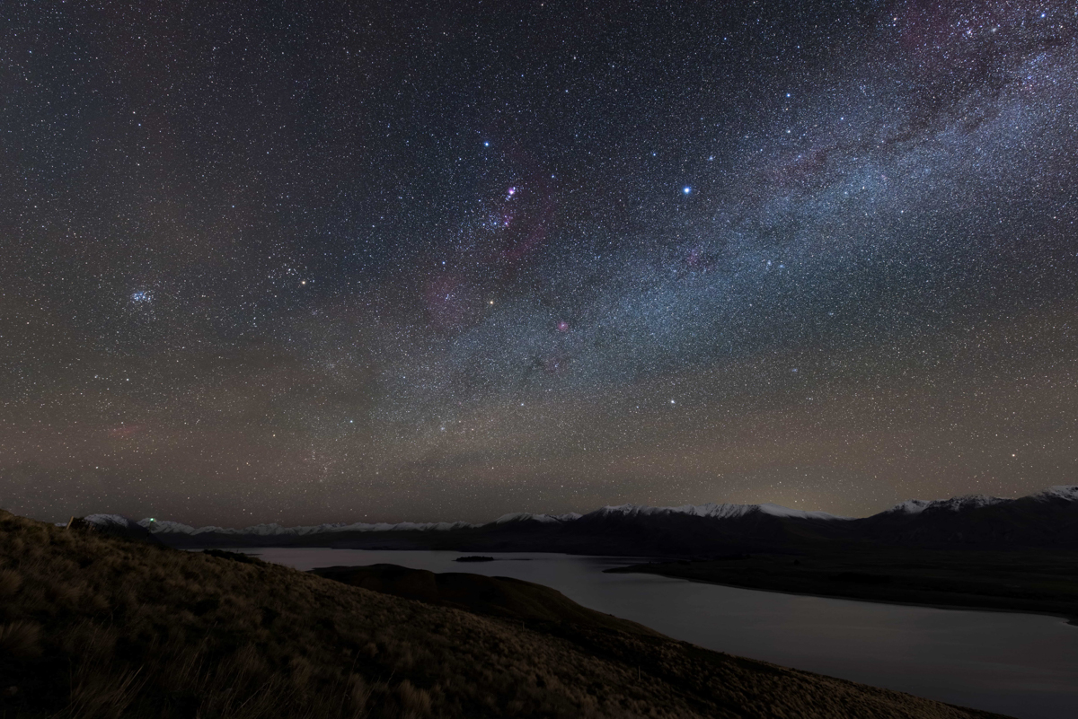 View across Lake Tekapo to snowcapped mountains with milky way